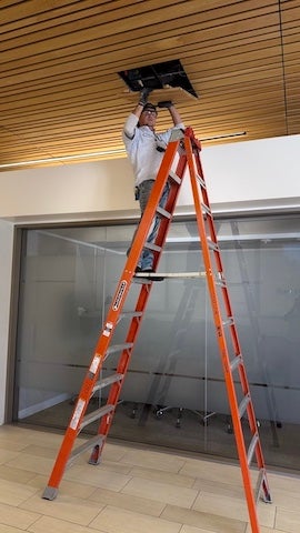 electrician at the top of a ladder removing a ceiling tile