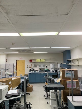 Laboratory with equipment, shelves, and boxes under fluorescent lights.